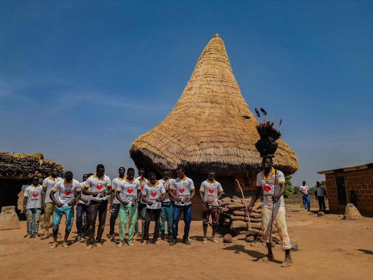 A welcome in a northern village: residents gathered in front of a thatched-roof hut